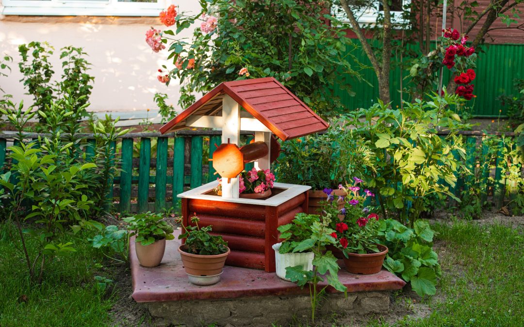 Puits décoratif en bois entouré de massifs fleuris et de plantes en pot dans un aménagement de jardin à Belleville